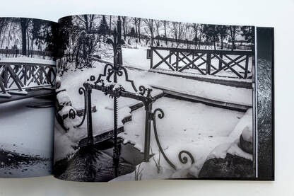 Schnee bedeckter Wasserlauf vom „Villateich“ mit Brücke und Zaun in Schwarz-Weiß.