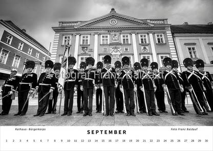 Schwarz-weiß Fotografie des privilegierten uniformierten Bürgerkorps vor dem Wiener Neustädter Rathaus im September, das die Mitglieder in traditionellen Uniformen und die historische Architektur des Rathauses zeigt.